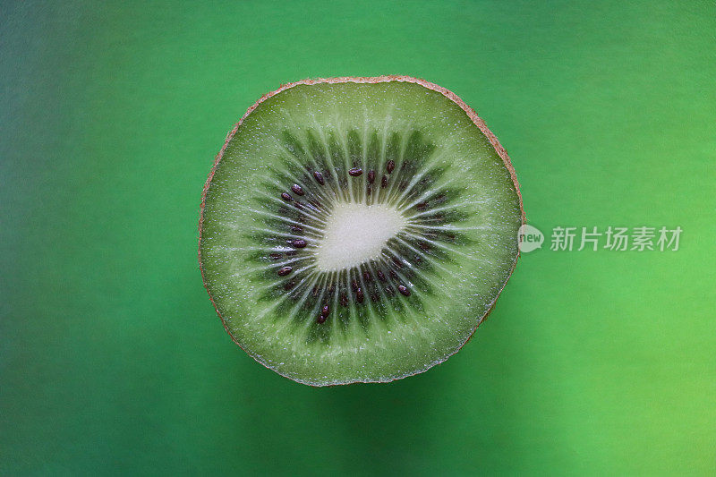 猕猴桃/中国猕猴桃(Actinidia chinensis)的特写图片，切成两半，显示模糊的棕色皮肤和亮绿色的果肉，黑色的种子环，斑驳的绿色背景，高架视图